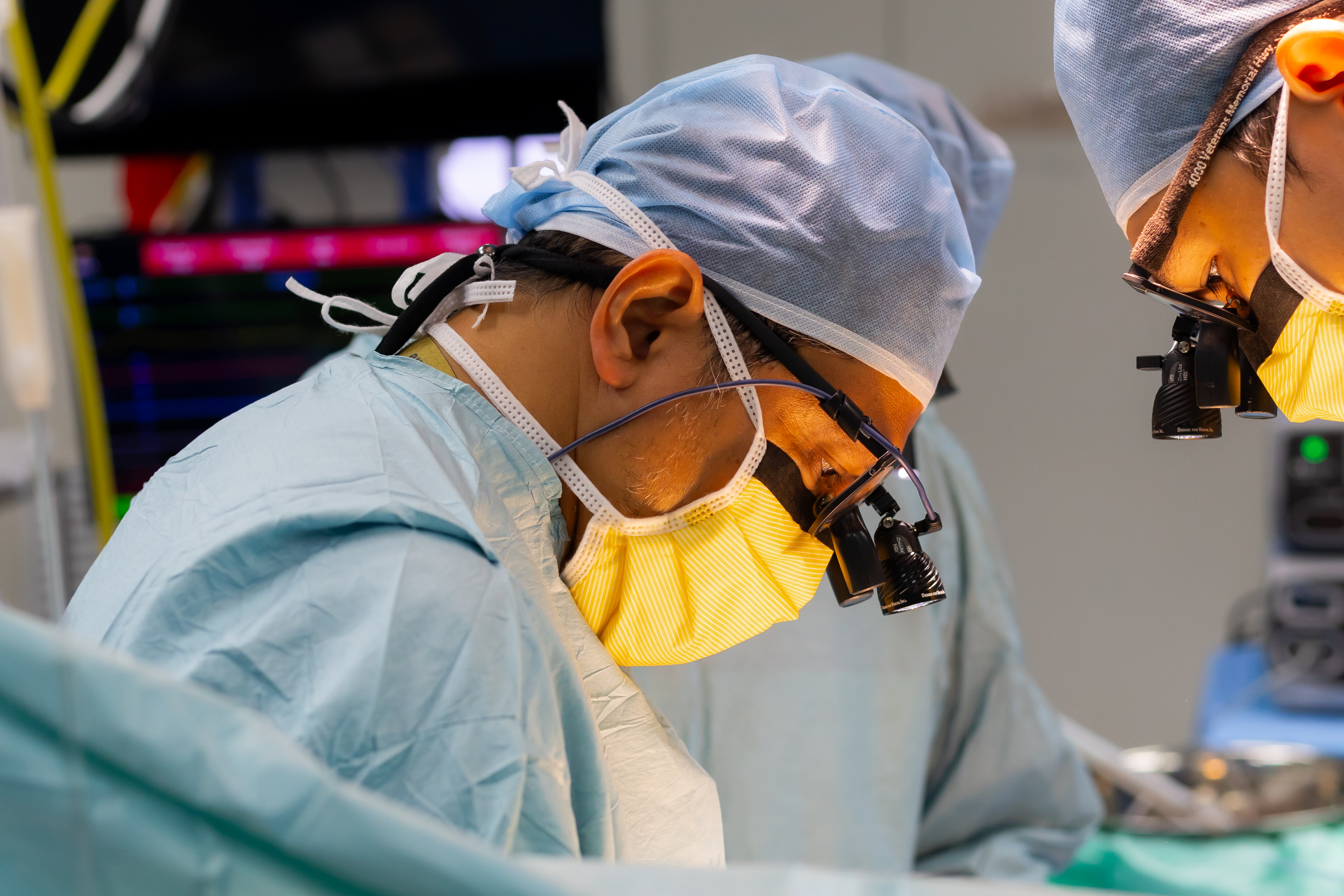 Close-up of Prof. Dr. Shahrul Amry Hashim in concentrated focus during a minimally invasive cardiac procedure, surgical loupes visible