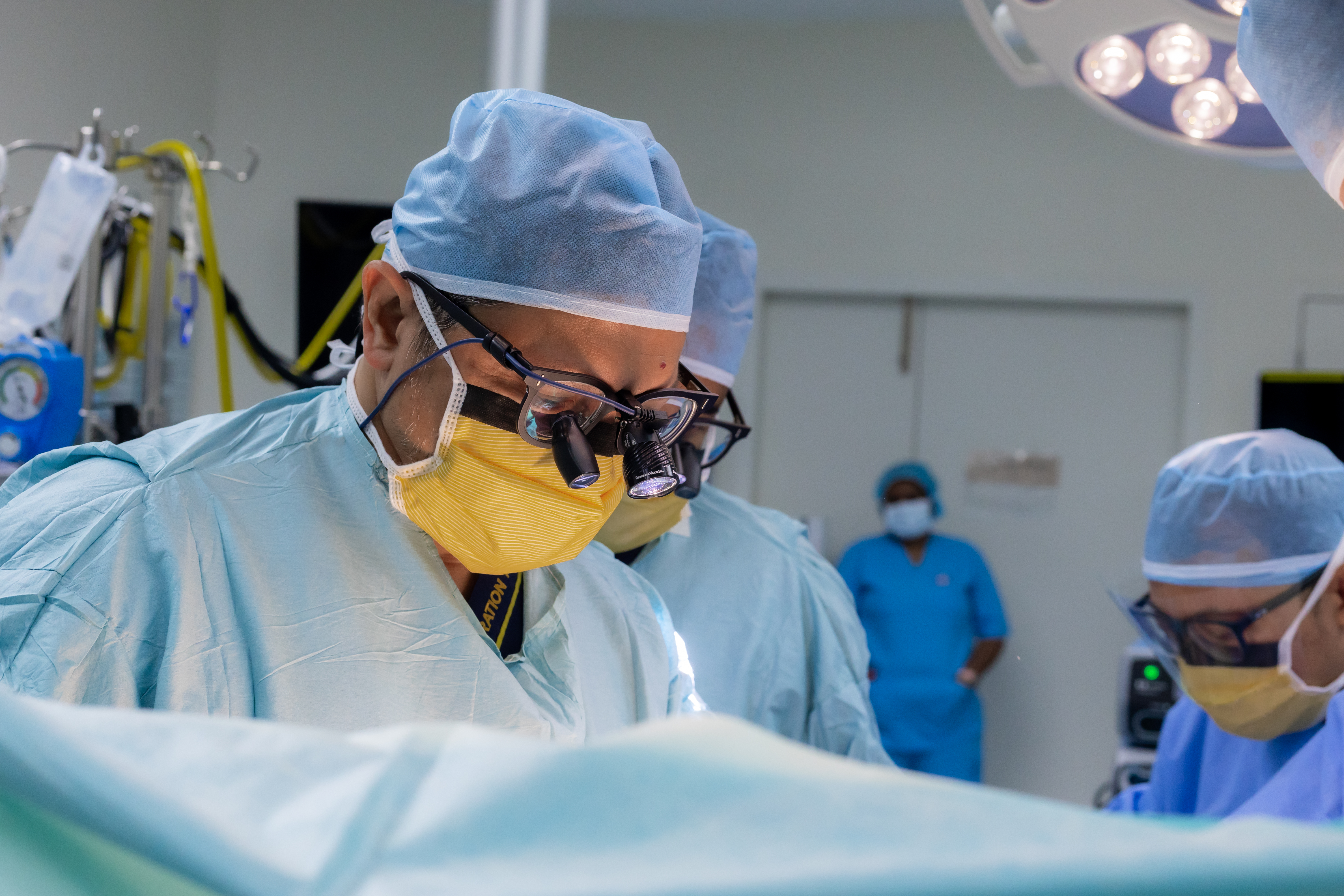 Prof. Dr. Shahrul Amry Hashim in the cardiac operating theatre at KPJ DSH2, focused over the surgical field with theatre lights above
